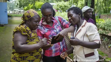 Three women are kooking at a smartphone, one holding another phone in her hand